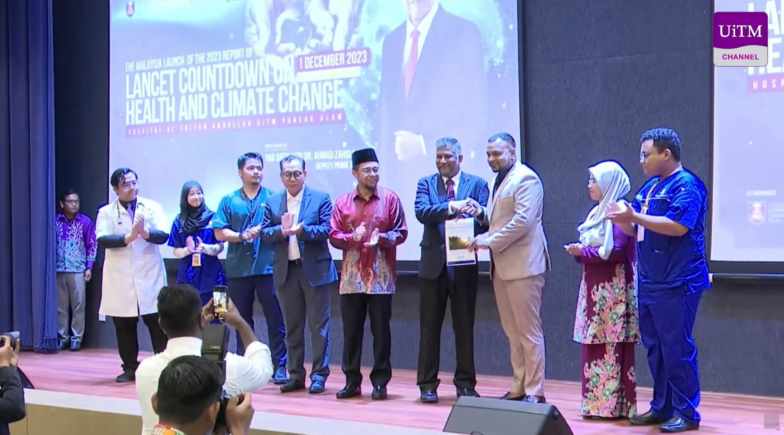 People on stage at an event with a screen showing “Lancet Countdown on Health and Climate Change” and UiTM logo.